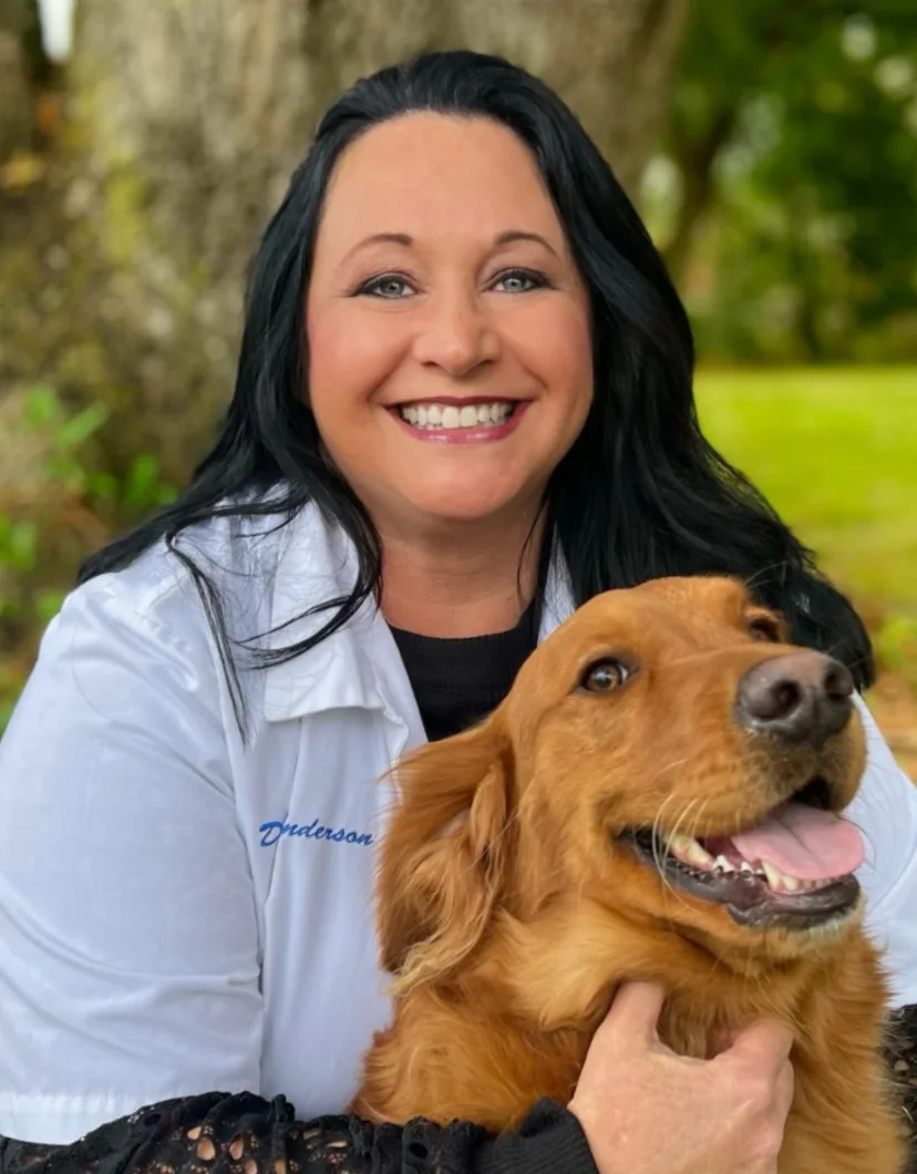 Dr. Agnes Clay-Anderson's Staff photo from Spanish Trail Animal Hospital where she is sitting outside hugging a big black dog